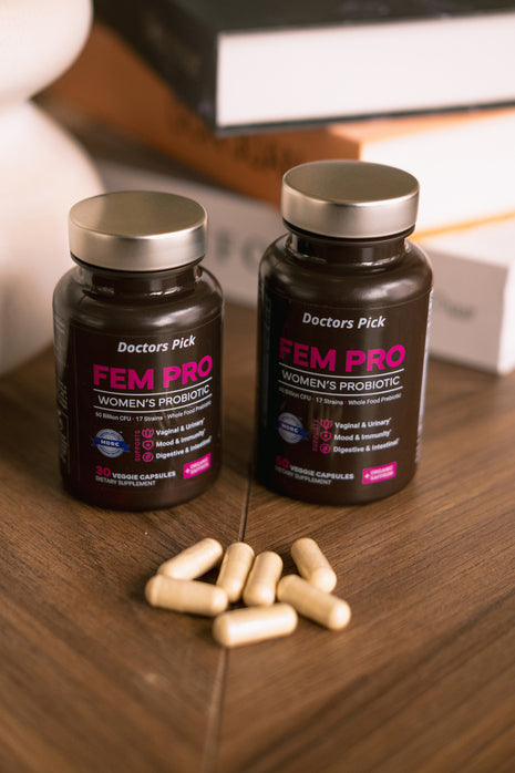Two bottles of 'Doctors Pick FEM PRO Women's Probiotic' on a wooden surface with scattered capsules.
